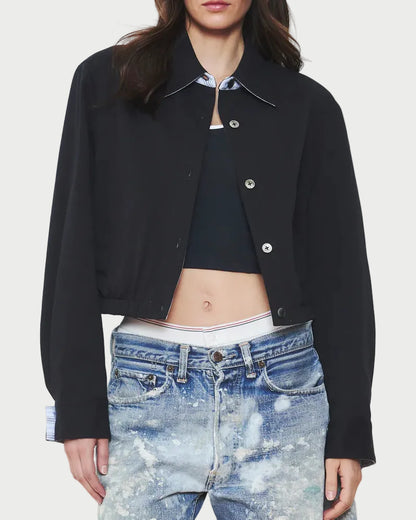 Woman wearing a black jacket and blue denim shorts on a plain background