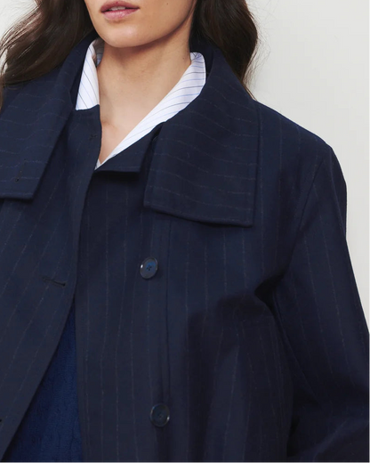 A woman models the WE-AR4 Kent Jacket by WE-AR4—a navy pinstripe upcycled wool jacket—layered over a crisp white collared shirt. Only her lower face and upper torso are visible against a plain, light-colored background.