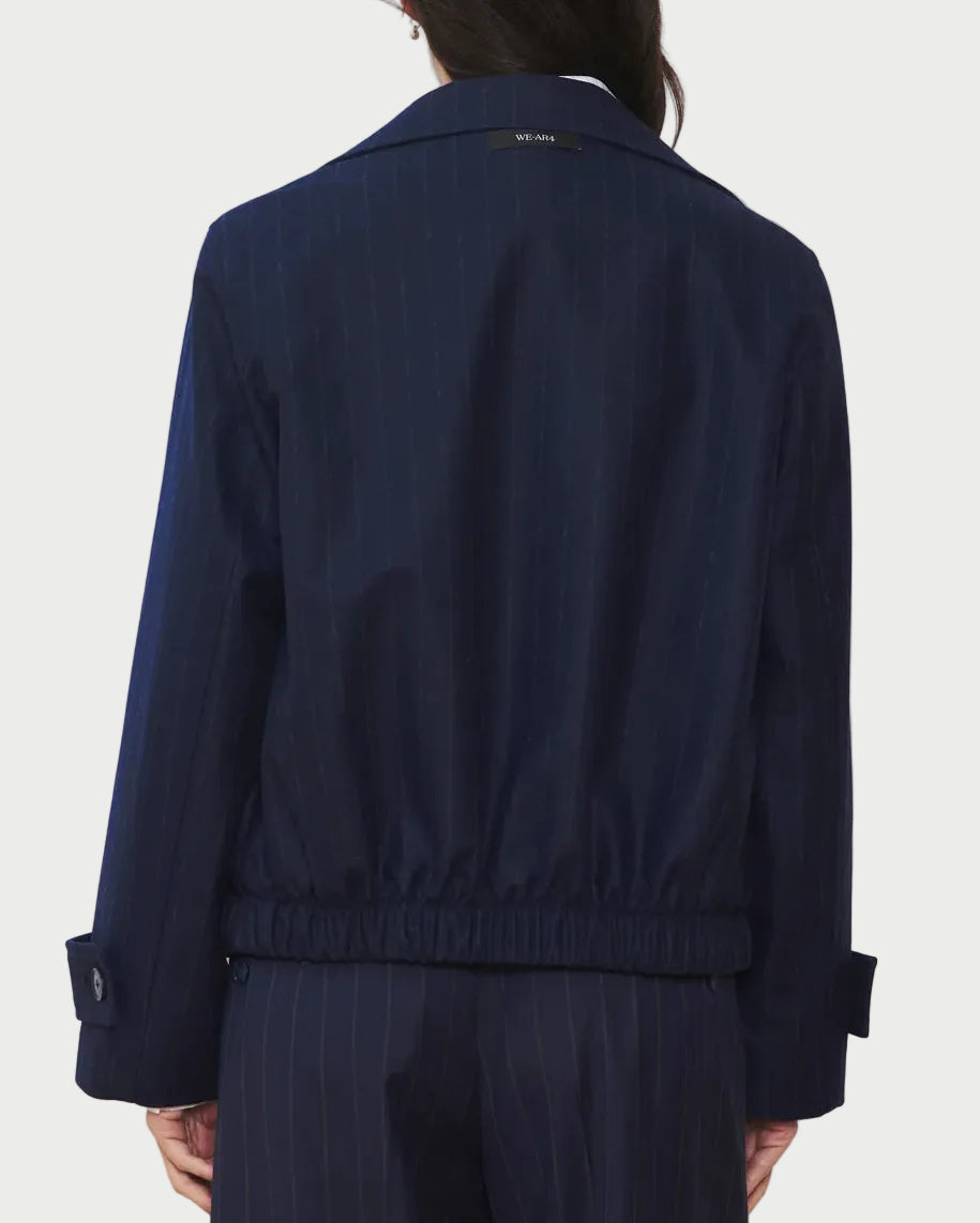 A person wearing the WE-AR4 Kent Jacket by WE-AR4 in navy blue pinstripes, paired with matching pants, shown from the back. This limited edition jacket features an elastic waistband and buttoned cuffs.