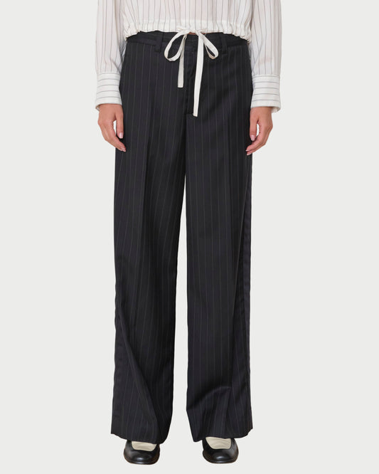 Person wearing black pinstripe pants with a white shirt against a white wall.