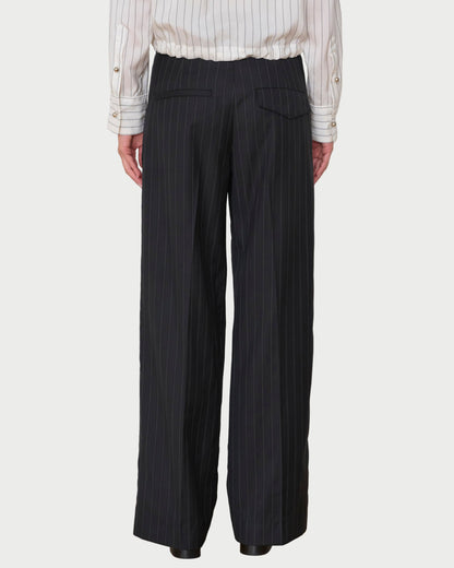 Person wearing black pinstripe pants and a white shirt against a white wall.