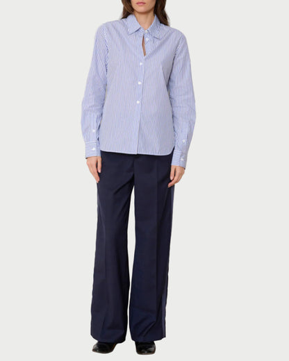 Woman wearing a blue and white striped shirt and navy pants against a white wall.