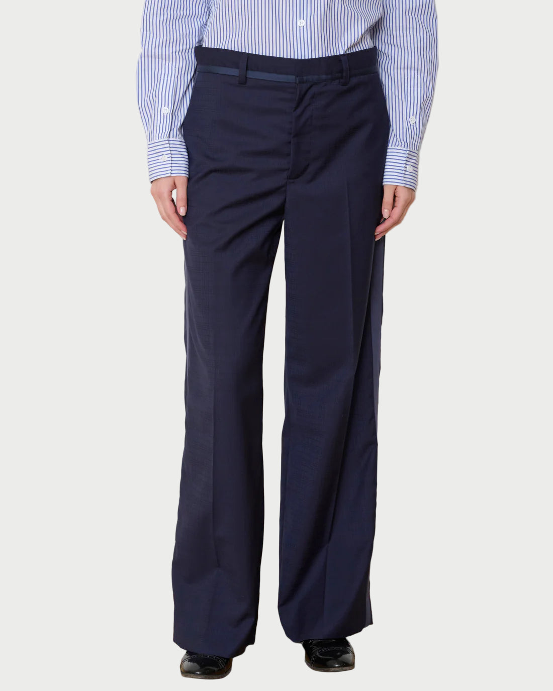 Person wearing navy pants and a striped shirt against a white wall.