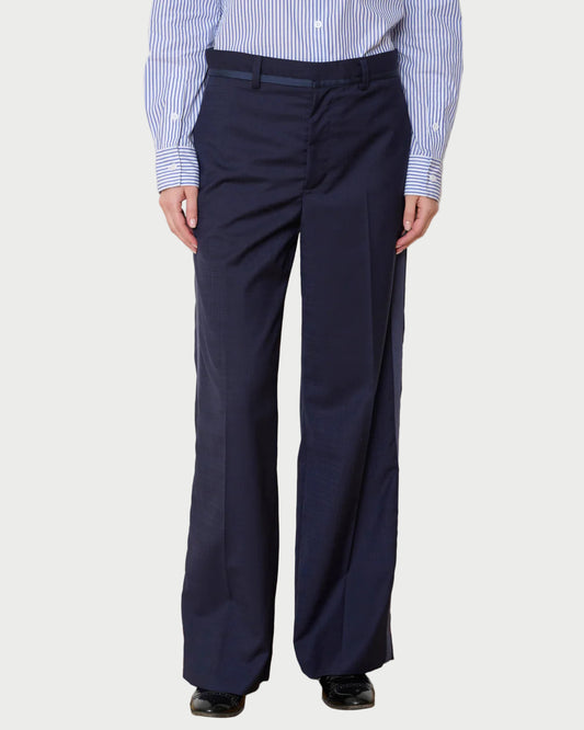 Person wearing navy pants and a striped shirt against a white wall.