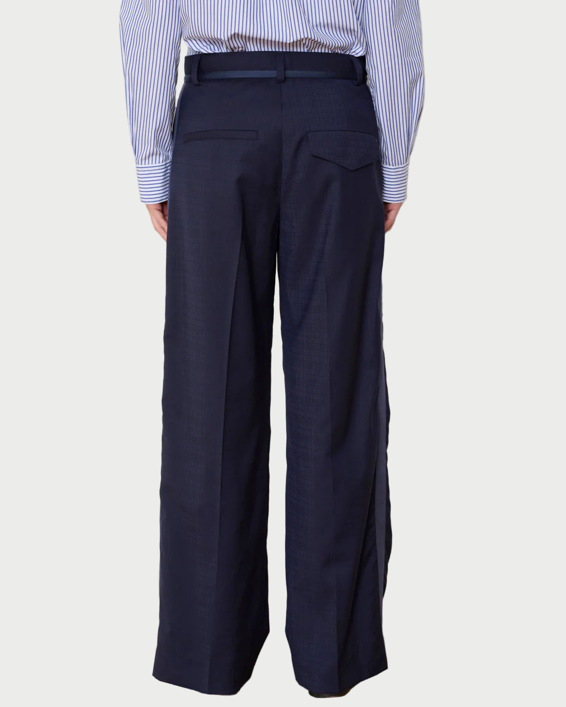 Person wearing navy wide-leg pants and a striped shirt against a white wall.