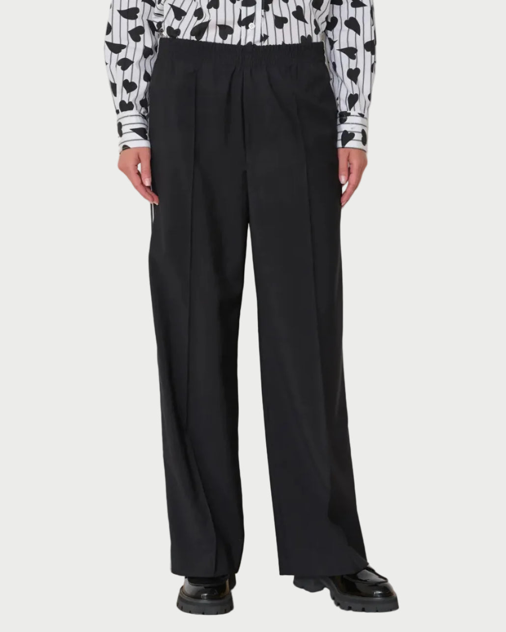 Person wearing black wide-leg pants with a patterned top against a white wall.