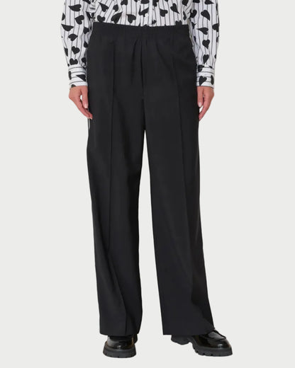 Person wearing black wide-leg pants with a patterned top against a white wall.