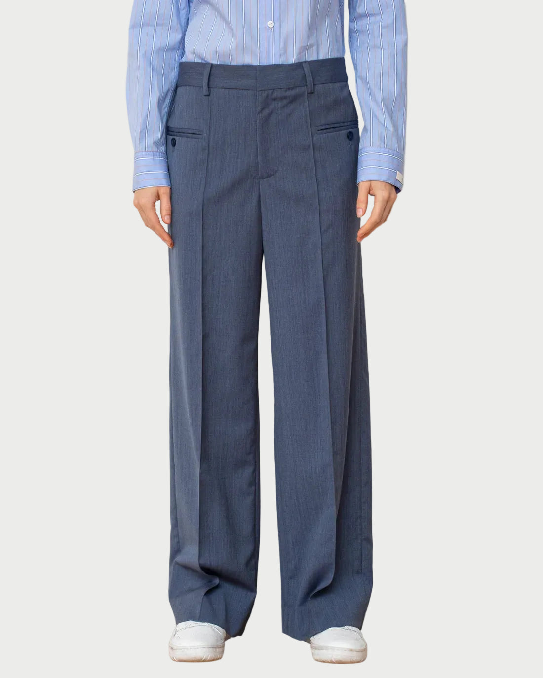 Person wearing a light blue shirt and dark gray pleated pants on a plain background