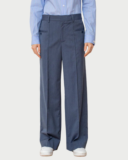 Person wearing a light blue shirt and dark gray pleated pants on a plain background