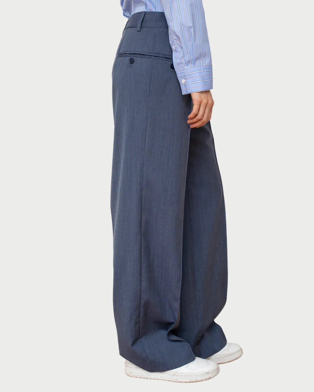 Person wearing blue wide-leg pants and a striped shirt against a white wall.