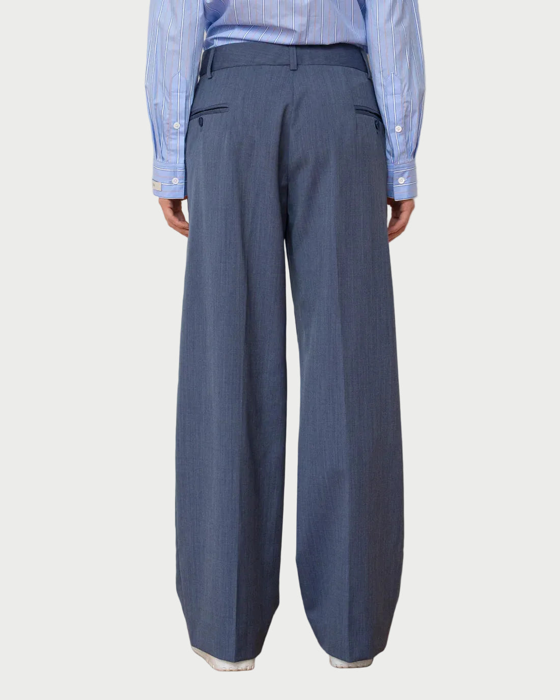 Person wearing a blue shirt and wide-leg gray pants against a white wall.