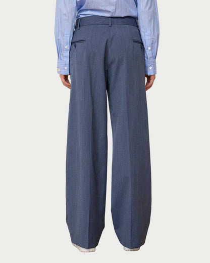 Person wearing a blue shirt and wide-leg gray pants against a white wall.