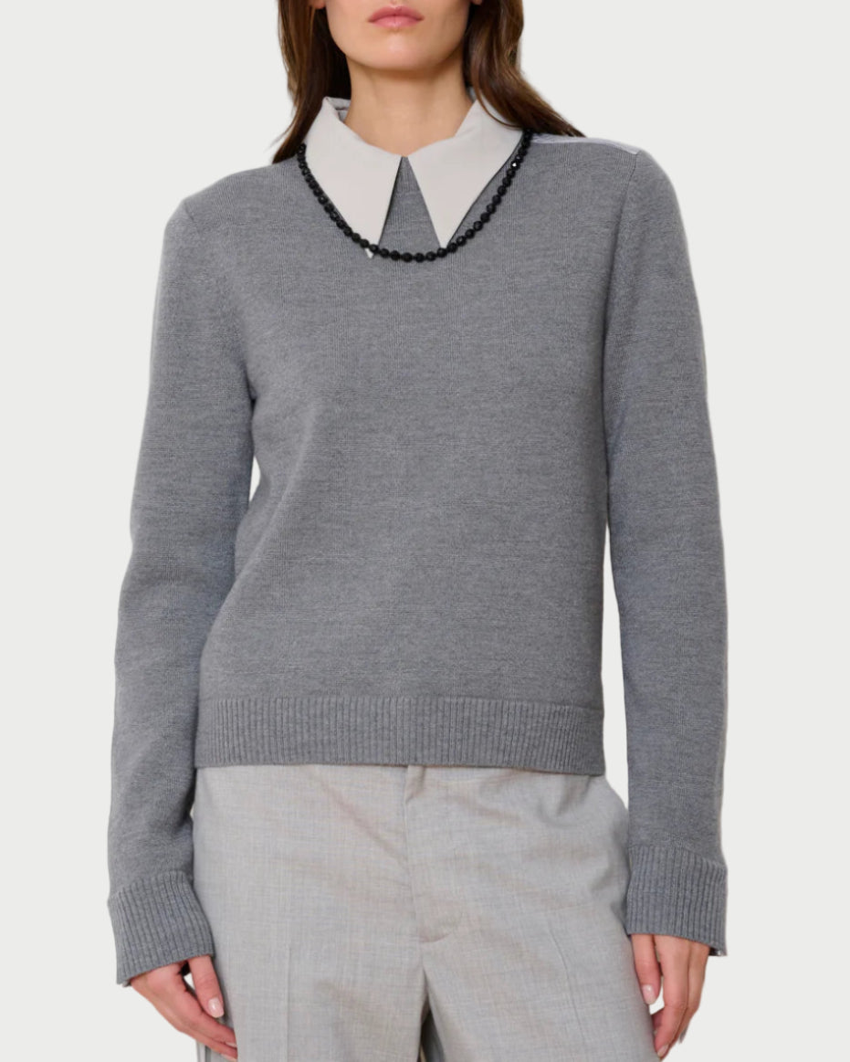 Woman wearing a gray sweater with a white collar against a plain background