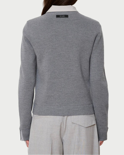 Person wearing a gray sweater with a visible brand logo on a white background