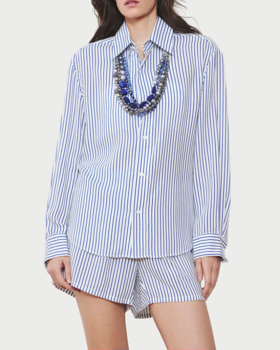 Woman wearing a blue and white striped shirt and shorts set with a necklace on a plain background