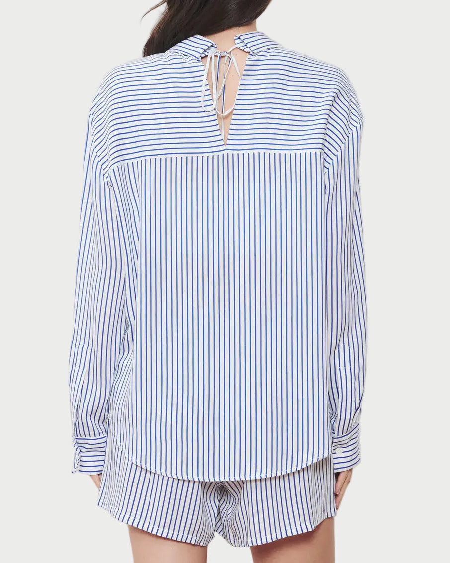 Woman wearing a blue and white striped shirt with a tie-back detail on a plain background