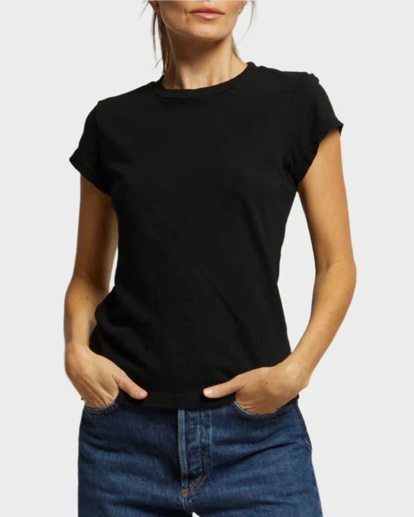 A woman stands with her hands in her pockets against a light background, wearing the perfectwhitetee Sheryl Basic Tee in black and blue jeans. Her face is partially out of frame.