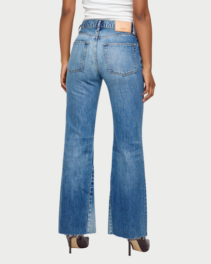 A person is seen from the back wearing the Moussy Asheville Flare Jean by Moussy, a pair of vintage-inspired low-rise flare jeans with frayed hems, crafted in Japan. The jeans feature large back pockets and a tan label on the waistband. The outfit is completed with dark heels and a white top.