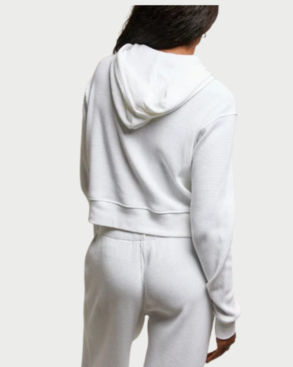 Person wearing a white hoodie and pants set on a plain background