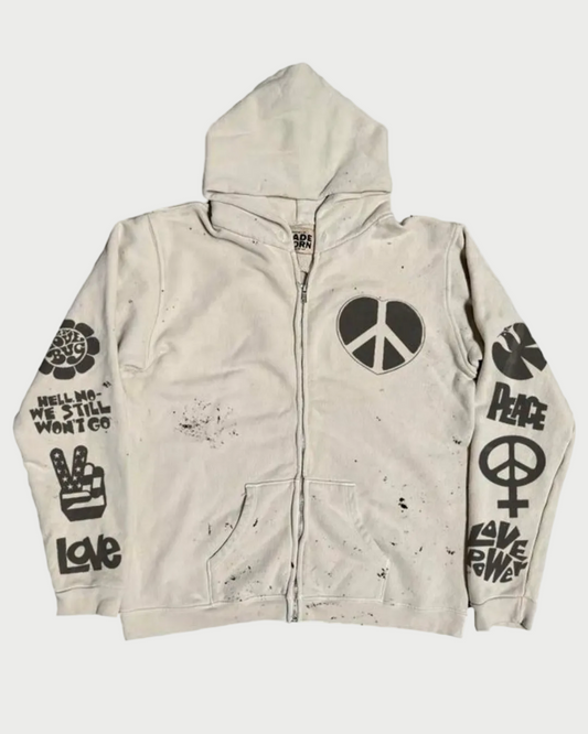The Madeworn "Love Trip" Zip Up Hoodie by Madeworn is a vintage white zip-up with a hood, black peace symbols, "Peace" and other peace-themed text, psychedelic graphics on front and sleeves, and bold black splatter marks.