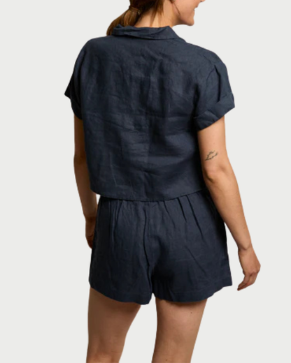 A person is seen from the back wearing the perfectwhitetee Tabitha Buttondown Collared Tee by perfectwhitetee, paired with matching shorts. Their brown hair is tied back, and a small tattoo is visible on their upper left arm.