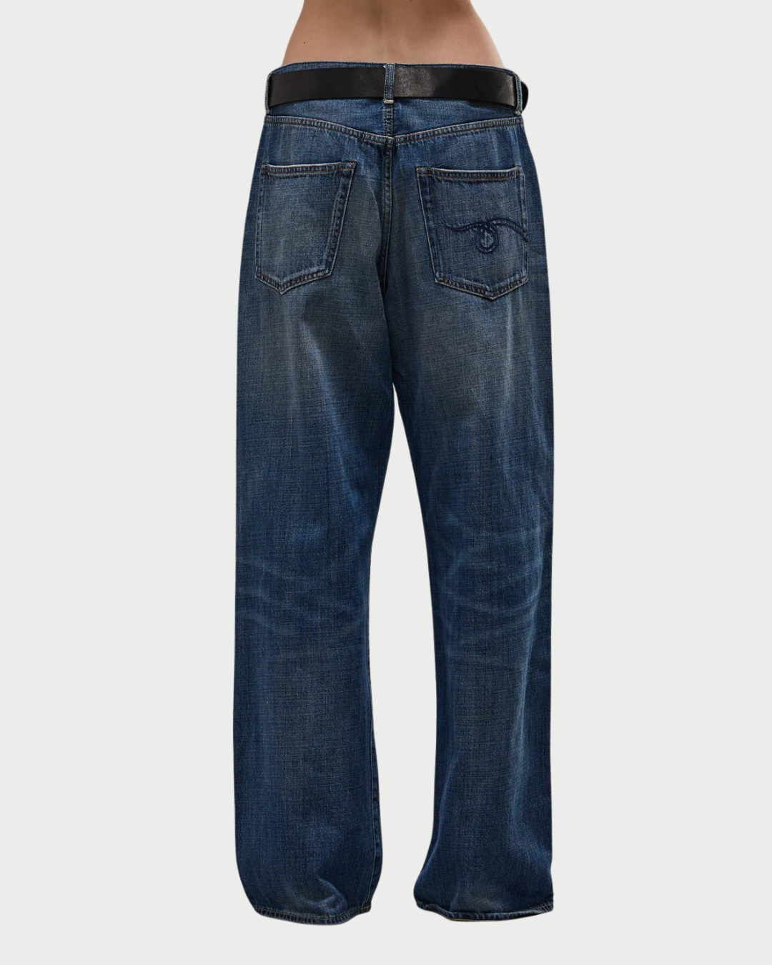 A person wearing R13 D'Arcy Loose Jean by R13—vintage-inspired, loose-fitting blue mid-rise jeans with a black belt, two back pockets (one with stitched design)—is seen from the back against a plain white background.