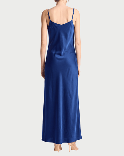 A woman shown from the back wearing a long royal blue satin slip dress with thin spaghetti straps, paired with beige high heels, against a light gray studio background.