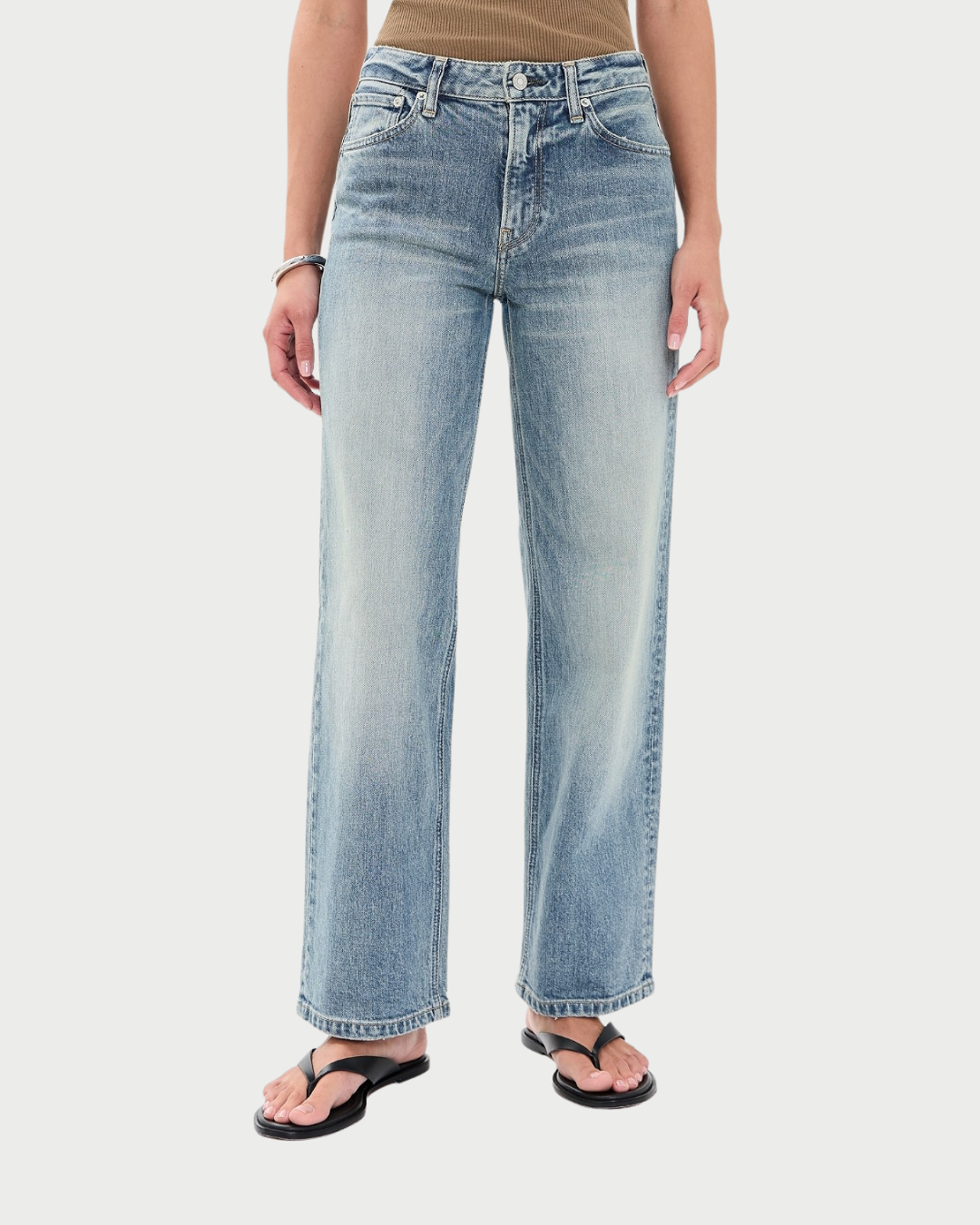 A person wearing light-wash blue straight-leg jeans with a faded wash, paired with black flip-flop sandals and a tan top, shown against a light gray studio background.