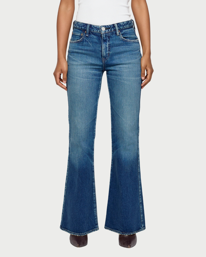 A model wearing a pair of medium-wash blue denim flare jeans, shown from the waist down against a light gray studio background.