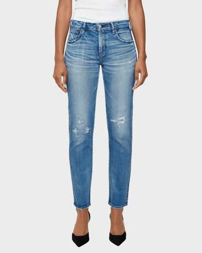 A model wearing a pair of medium-wash blue denim jeans with distressed details on the thighs and knees, paired with a white top and black heels, against a light gray background.