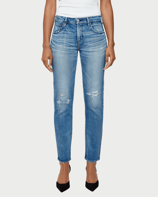 A model wearing a pair of medium-wash blue denim jeans with distressed details on the thighs and knees, paired with a white top and black heels, against a light gray background.