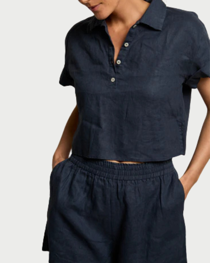 A person wears the perfectwhitetee Tabitha Buttondown Collared Tee in dark navy with matching high-waisted elastic shorts, standing with one hand in a pocket.