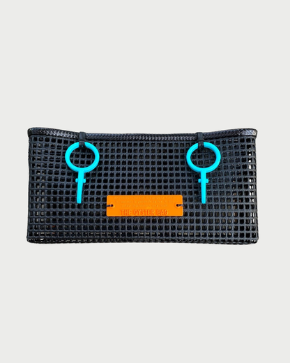 The Oyster Bag The Clutch by THE OYSTER BAG is a rectangular black mesh waterproof beach bag with two blue circular plastic handles and an orange front label reading "THE OYSTER BAG," shown against a plain white background.