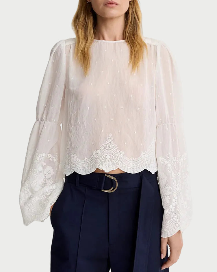 Woman wearing a white lace blouse and navy pants on a white background