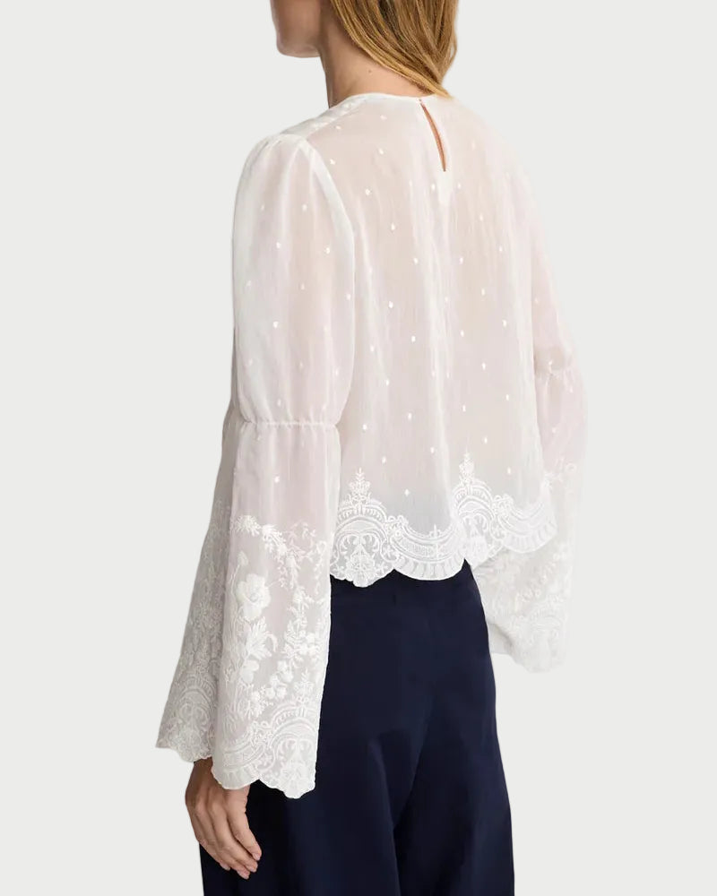 Woman wearing a white lace-trimmed blouse and dark pants on a plain background