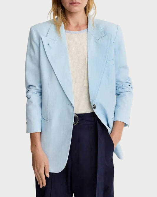 Woman wearing a light blue blazer over a beige top and dark pants on a white background