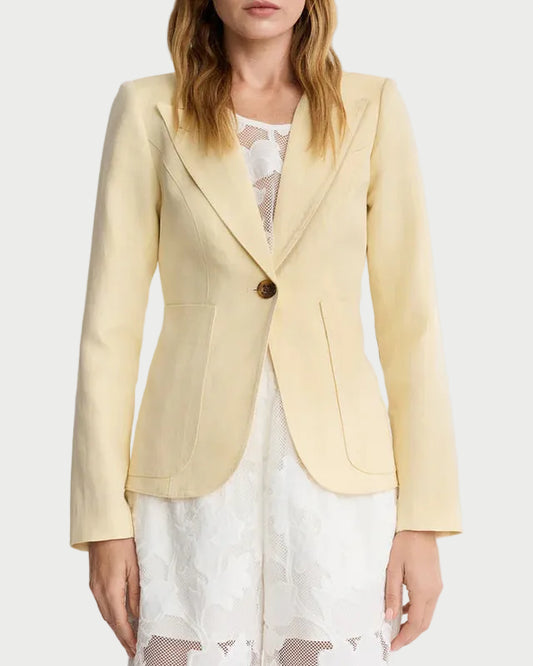 A woman stands against a plain background wearing the Smythe Patch Pocket Duchess Blazer in light yellow over a white lace dress. The tailored Smythe blazer features leather elbow patches, patch pockets, a single button, and notched lapels.
