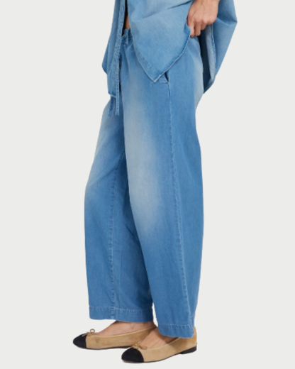 A person wearing SPRWMN Helena Drawstring Pants, a matching blue top, and beige flats with black toe caps stands against a white background.