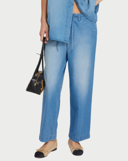 A person wearing SPRWMN Helena Drawstring Pants, a matching denim shirt, tan and black ballet flats, and carrying a small black handbag with animal print sides.