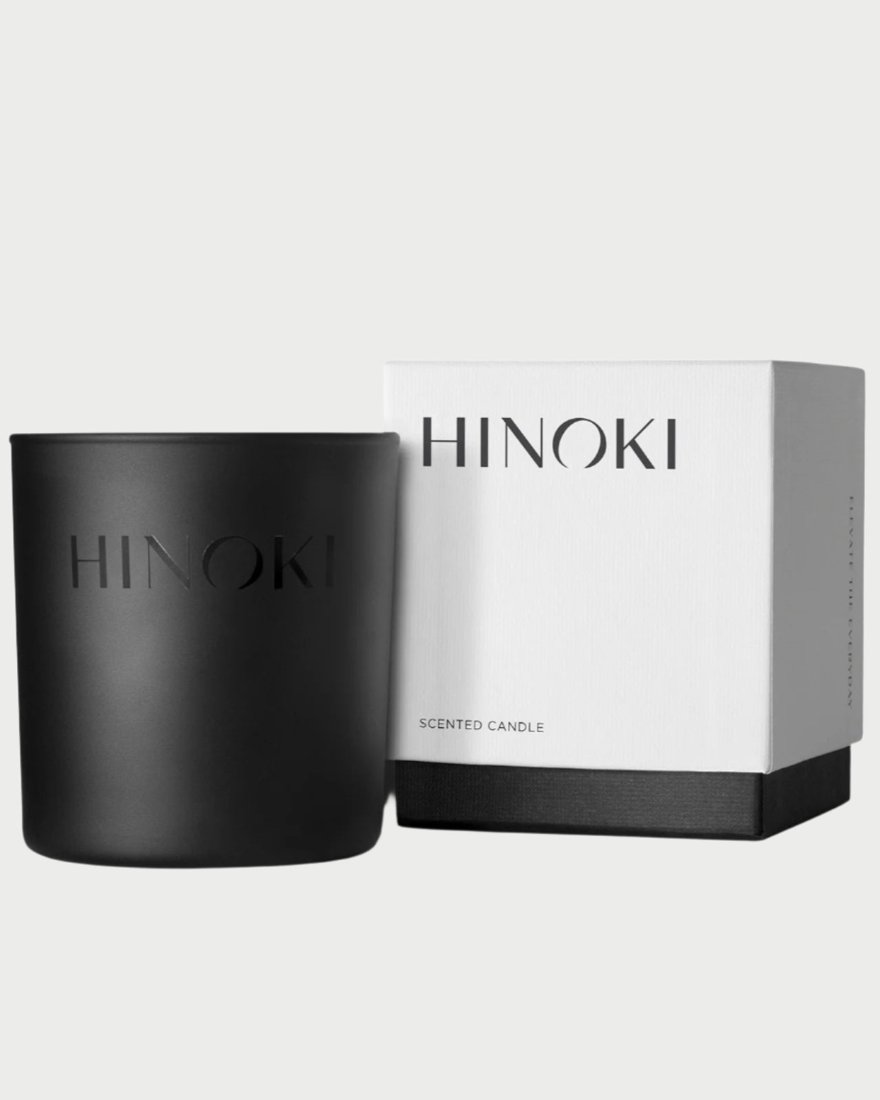 Black Hinoki scented candle next to its white box on a white background