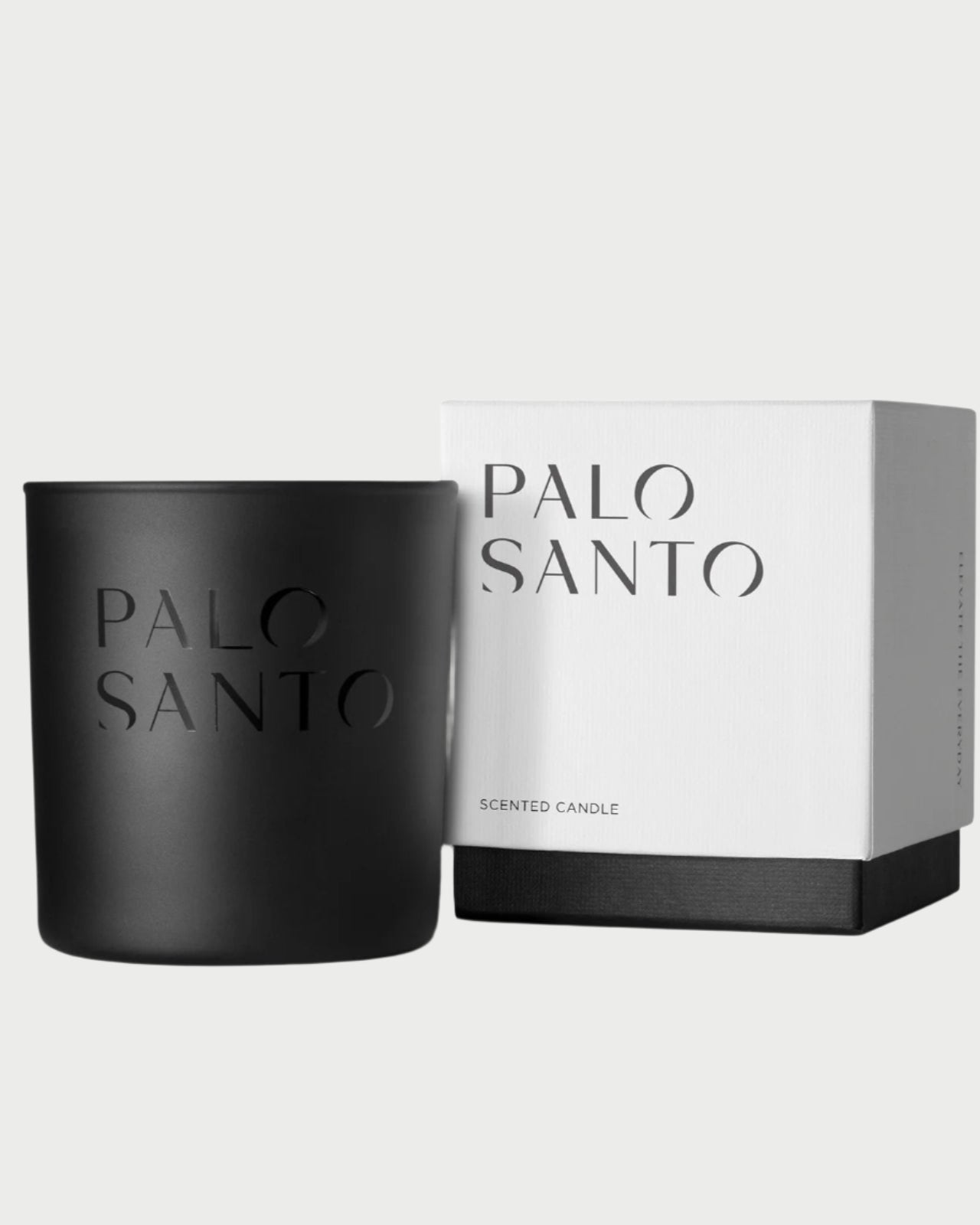 A black Studio Stockhome Palo Santo Candle sits beside a matching white and black box labeled "PALO SANTO" and "SCENTED CANDLE"—luxury natural soy candles from Studio Stockhome on a plain light background.