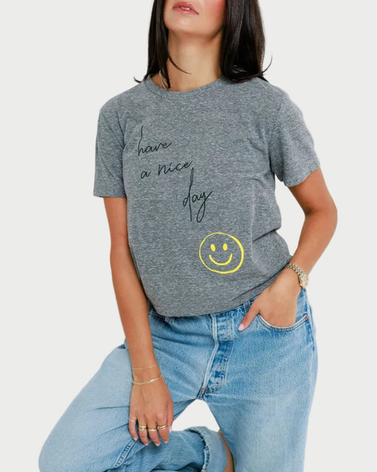 Woman wearing a gray t-shirt with text and a smiley face, standing against a white background