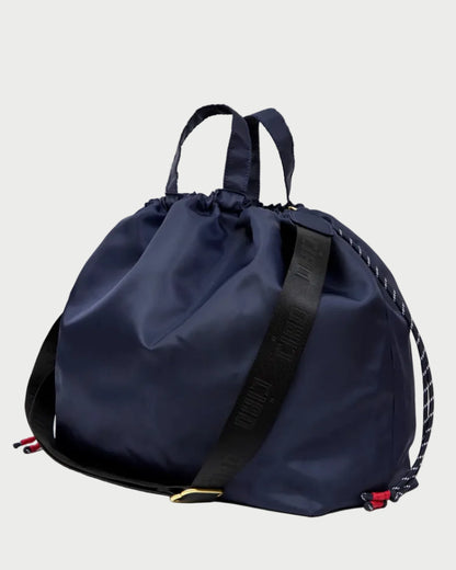 A navy blue nylon drawstring backpack with a black webbed shoulder strap featuring white lettering, set against a plain white background.