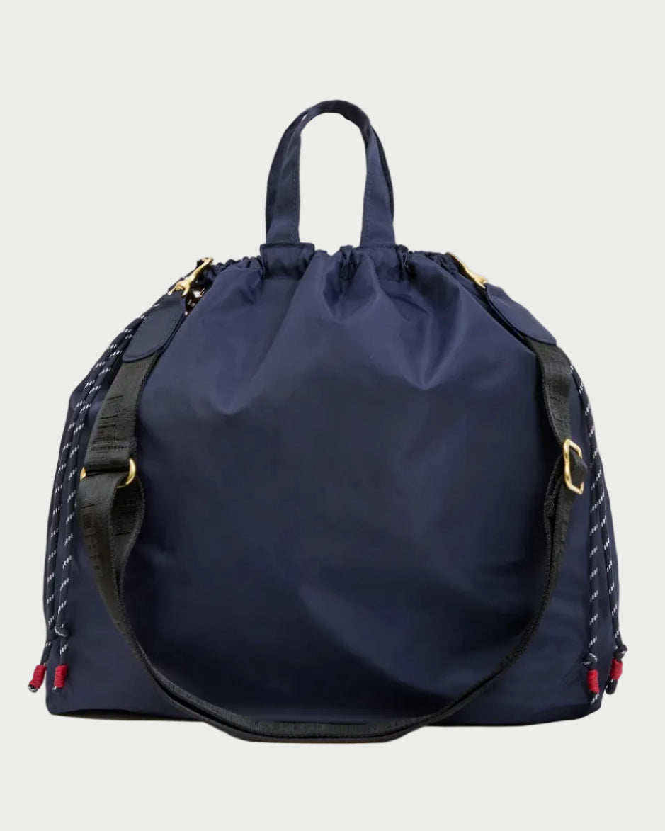 A navy blue nylon drawstring bag with black braided side straps, gold-tone hardware, and red and blue tassel accents, shown against a plain white background.