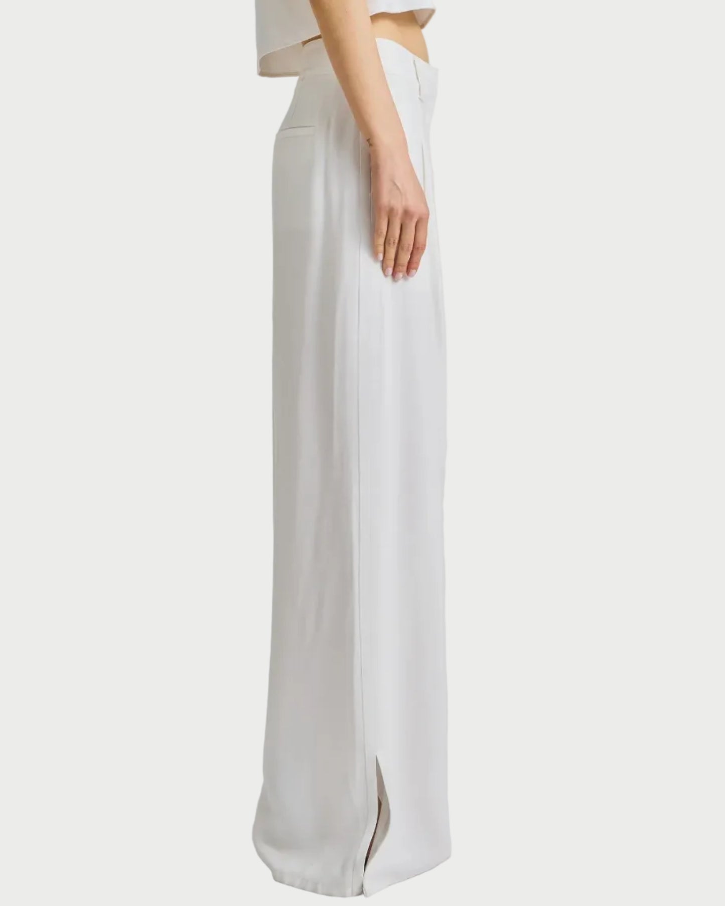 Woman wearing a white sleeveless top and wide-leg pants on a plain background