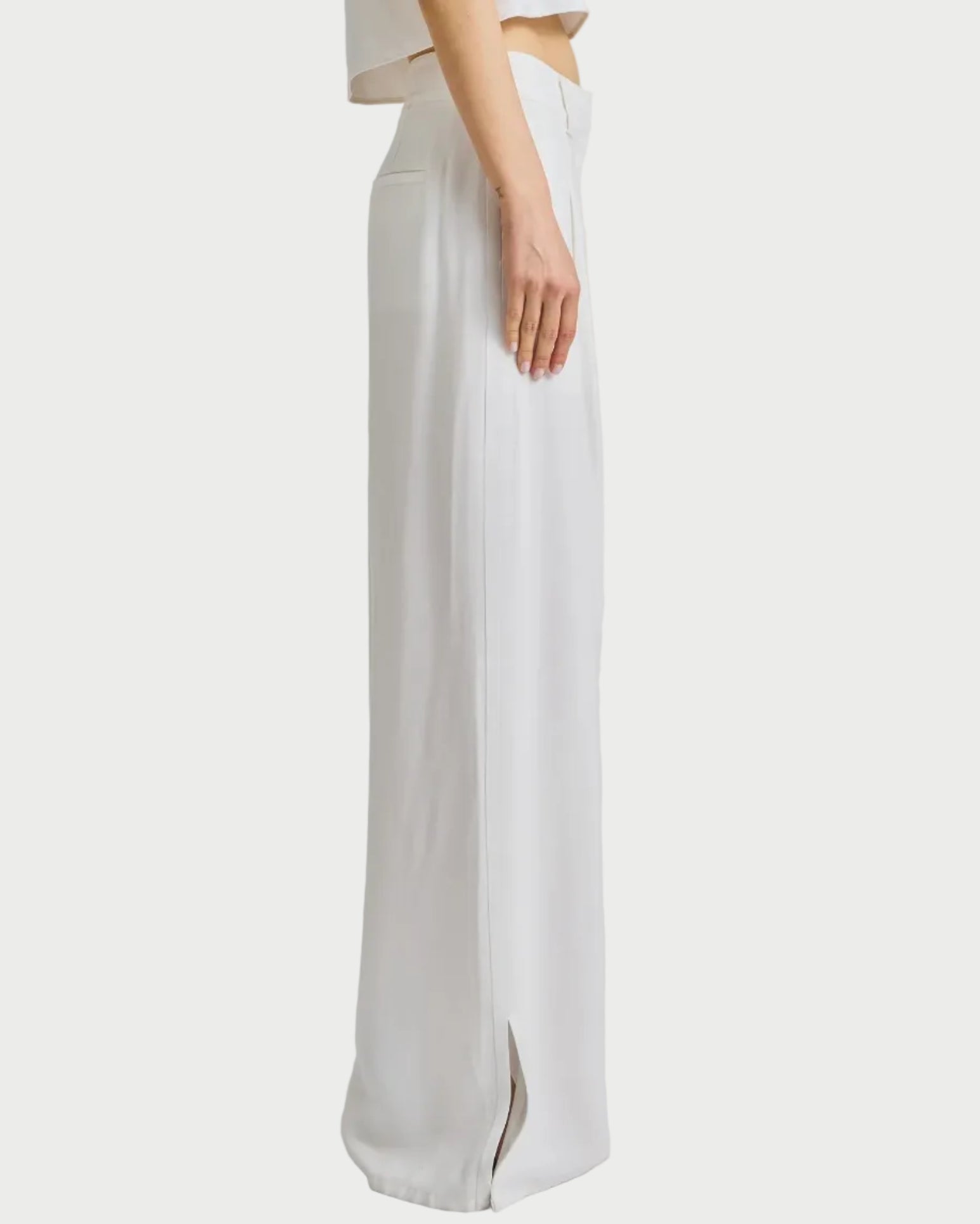 Woman wearing a white sleeveless top and wide-leg pants on a plain background