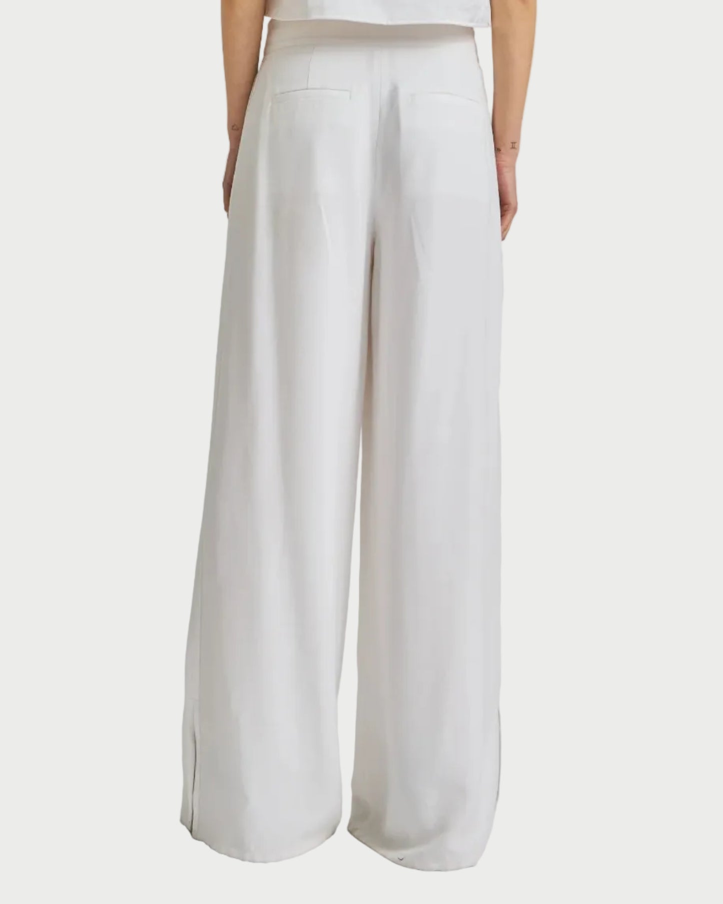 Woman wearing a white sleeveless top and wide-leg pants on a plain background