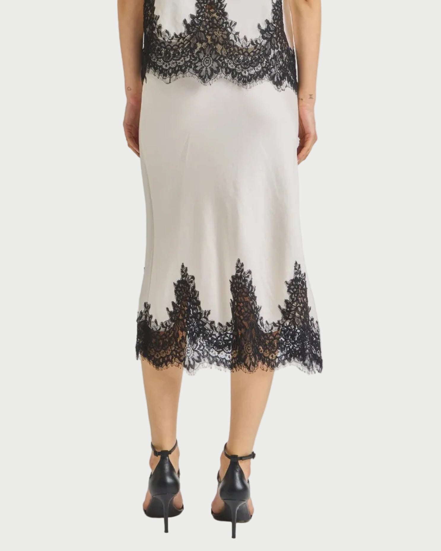 Woman wearing a white skirt with black lace details on a plain background