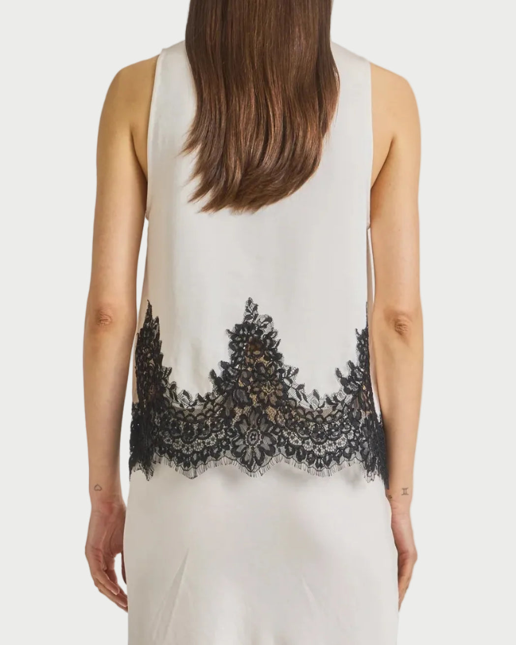 Woman wearing a sleeveless top with black lace details on a plain background