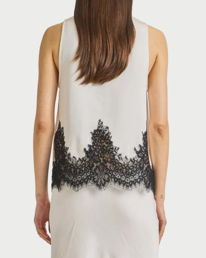 Woman wearing a sleeveless top with black lace details on a plain background